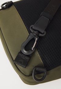 Green fabric bag featuring a black mesh section, a clip closure, and a loop for attachment. Smooth texture with contrasting materials.