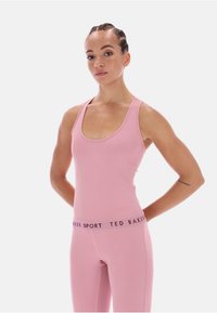 Roza aktivna majica brez rokavov s krožnim izrezom in ozkimi naramnicami, v kombinaciji z ustreznimi leggingi z elastičnim pasom z blagovno znamko.