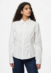 Camicia bianca da uomo in cotone, con colletto classico, maniche lunghe e una vestibilità aderente con una superficie liscia.