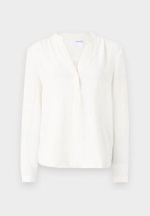 Witte blouse met lange mouwen, knoopsluiting, zachte textuur, iets losse pasvorm en ronde halslijn. Dunne manchetten aan de mouwen.