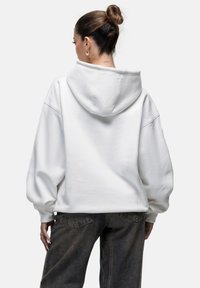 Witte hoodie met een grote capuchon, relaxte pasvorm, verlaagde schouders en ribgebreide manchetten, gecombineerd met donkere spijkerbroeken.