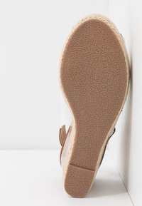 Semelle d'une sandale compensée blanche avec semelle en caoutchouc brun texturé et semelle intermédiaire en jute tressé, taille 4, positionnée sur des surfaces blanches.