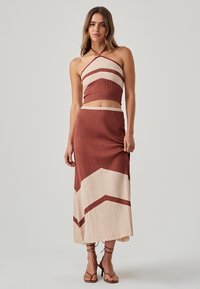 Set a due pezzi a coste composto da un top corto con collo halter e una gonna. I colori includono ruggine e crema, con un motivo a chevron. Il materiale sembra morbido.