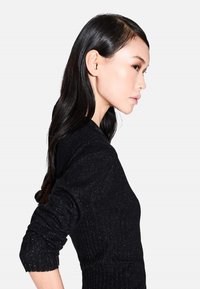 Zwarte gebreide trui met een geribbeld patroon, voorzien van een diepe V-hals en aansluitende mouwen. De stof heeft een metallic draad voor een glinsterend effect.