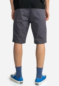 Pantaloni corti in cotone grigio con una vestibilità comoda, di lunghezza media fino alla coscia. Abbinati a sneakers blu e calzini a costine, che mostrano uno stile casual.