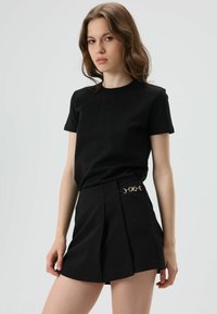 T-shirt noir à manches courtes associé à un short noir taille haute agrémenté d'un détail en chaîne métallique à la taille. Texture de tissu lisse.
