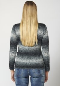 Harmaa neulepaita, jossa on liukuvärillinen kuvio, pitkät hihat ja teksturoitu viimeistely. Yhdistetty sinisiin farkkuihin.