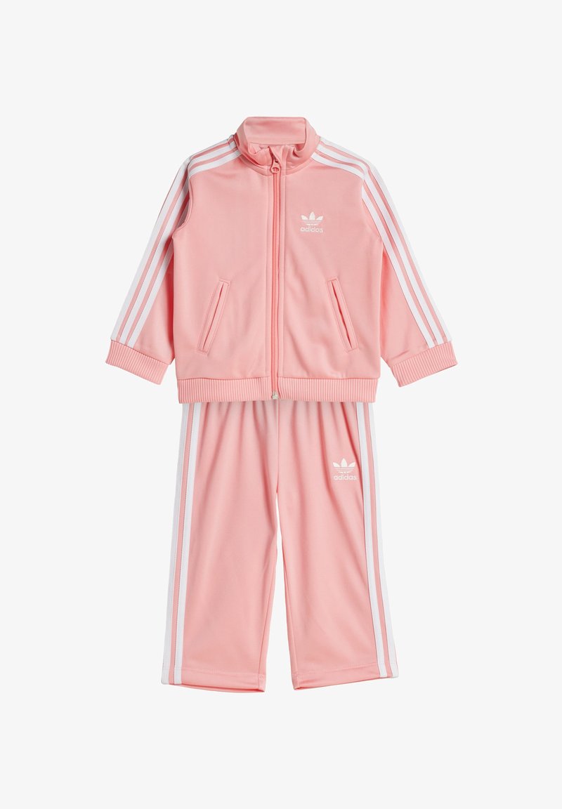 Ροζ φόρμα με λευκές ρίγες, που περιλαμβάνει ζακέτα με φερμουάρ και ψηλό γιακά καθώς και δύο τσέπες, συνδυασμένη με παντελόνι με ελαστική μέση.