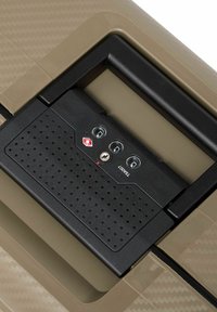 Harde koffer met een gestructureerd kaki oppervlak. Kenmerkt een zwart, TSA-goedgekeurd vergrendelmechanisme met drie schakelaars en een sleuf voor een sleutel.