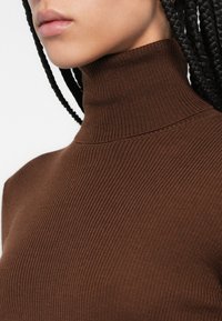 Pull à col roulé marron côtelé avec un col haut et une coupe ajustée, fabriqué dans un matériau doux et extensible.