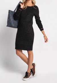 Robe en tricot noire avec des paillettes dorées, à manches longues et texture côtelée, assortie à un tote gris et des sneakers à imprimé léopard.