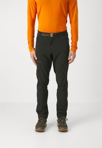 Celana outdoor hitam dengan potongan slim, dilengkapi dengan saku gesper samping dan ikat pinggang. Model mengenakan kaos lengan panjang berwarna oranye dan sepatu.