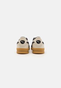 Puma-Sneaker aus cremefarbenem und schwarzem Leder mit einer Gummisohle. Merkmale sind das Logo an der Ferse und Mesh-Details an den Seiten. Niedrig geschnittenes Design.