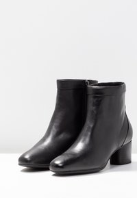 Stivaletti alla caviglia in pelle nera con finitura liscia, punta arrotondata e tacco a blocco, dotati di cerniera laterale ed elementi di design minimalisti.