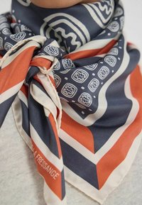 Foulard en soie avec un motif géométrique aux couleurs bleu marine, orange et crème ; noué autour du cou avec une texture douce.