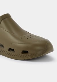 Shoe verde oliva de borracha com acabamento suave, apresentando furos de ventilação na parte superior e uma sola texturizada para aderência.