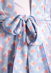 Gros plan d’un tissu à motifs bleu, blanc et rose noué en un nœud décoratif à la taille d’un vêtement.