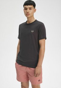 T-shirt in cotone nera con collo rotondo e maniche corte, caratterizzata da un piccolo logo ricamato sul lato sinistro del petto. Abbinata a pantaloni corti rosa.