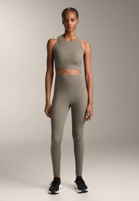 Sportos felső és leggings tompa olívazöld színben, sima, rugalmas anyagból készült, varrás nélküli kivitelben, ívelt varrási részletekkel.