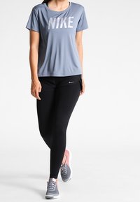 Grå Nike t-shirt med logotyp, kombinerad med svarta leggings och grå sneakers med rosa detaljer. Fokus på atletisk design och passform.