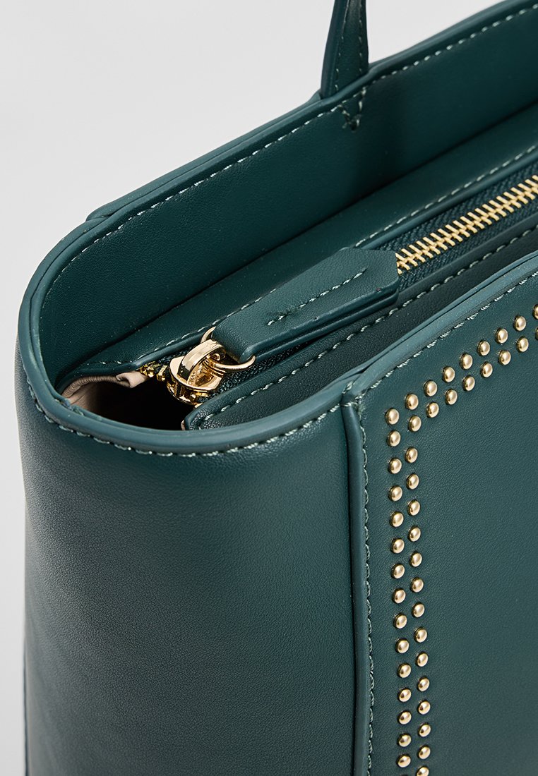 Grüne Lederhandtasche mit goldenen Nieten, Reißverschluss und glatter Textur. Verfügt über einen oberen Griff zum Tragen.