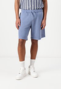 Blå bomulds shorts med elastisk talje, sidelommer og syet kant. Sammen med hvide sneakers og ribbede sokker.