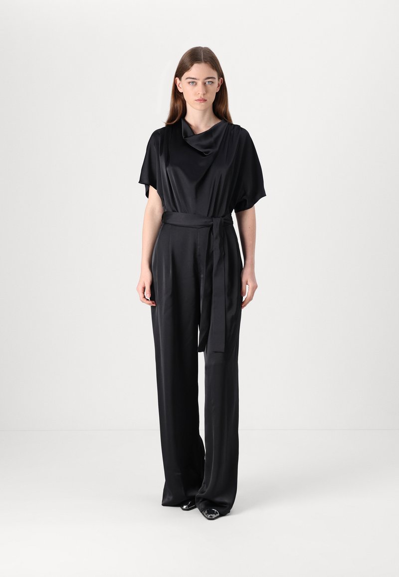 Svart sateng jumpsuit med vide ermer, en bølget hals, en figursydd midje med belte, og flytende, rette benbukser.