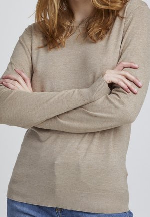 Pull en maille beige à manches longues, avec des poignets et un ourlet côtelés. Texture douce, coupe légèrement ajustée et motif légèrement moucheté.