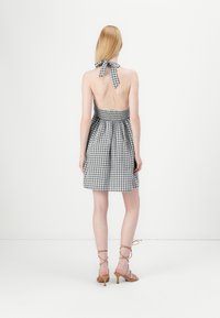 Rochie cu gât în formă de halter, în carouri alb-negru, cu bust elastic, spate deschis și fustă evazată, asortată cu sandale cu toc bej.