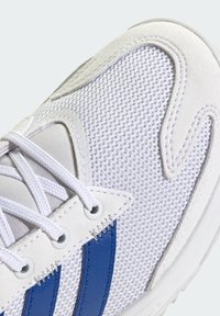 Baskets blanches avec un dessus en mesh respirant, rayures en cuir bleu et œillets ronds. Surface texturée avec des détails de couture contrastants.