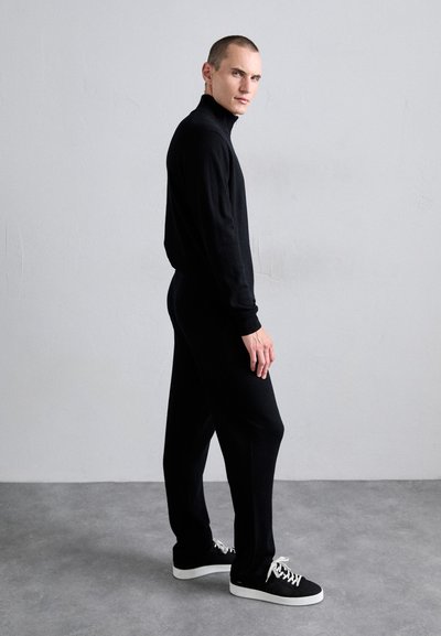 Black knit outfit with a high neck, featuring a fitted silhouette and long sleeves. Paired with black sneakers with white soles.