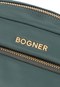 Grön nylonväska med ett guldblixtlås och varumärket "BOGNER" i guldtryck. Slät textur med en strukturerad design.