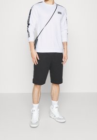 Vit sweatshirt med svarta accenter, i kombination med svarta shorts. Vita högskaftade sneakers; inkluderar en axelväska och logotyp på kläderna.