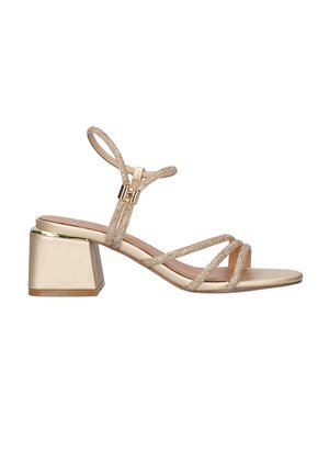 Sandalia con tacón bloque dorado, con tiras delgadas y brillantes y cierre de hebilla alrededor del tobillo, fotografiada sobre un fondo blanco.