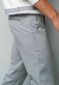Lichtgrijze broeken van een gladde stof, met een slim fit, subtiele zijzak en schone naden, gecombineerd met een witte gebreide trui.