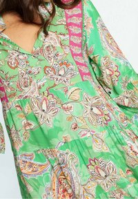 Vestido floral verde con un vívido patrón paisley, escote en V y acentos rosas en las mangas y el cuerpo. Textura de tela suave.