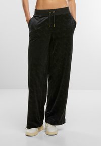 Schwarze Velours-Jogginghosen mit elastischem Taillenbund, Kordelzugverschluss und seitlichen Taschen; mit einem durchgehenden, geprägten Logomuster.