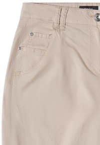 Pantalon beige clair avec poches avant, passants de ceinture, détails en rivets argentés et fermeture à bouton métallique à la taille.