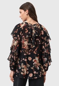 Blusa nera floreale con maniche a volant, un fiocco sul retro e un tessuto leggero e strutturato con motivi floreali rosa e crema.