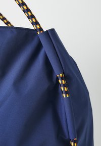 Sac en tissu bleu marine avec des poignées tressées ornées d'accents orange, jaune et noir. Texture lisse avec un design simple et arrondi.