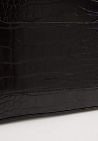 Borsa nera con texture di coccodrillo, caratterizzata da una finitura liscia e logo impresso. Il design presenta linee pulite e hardware minimale.