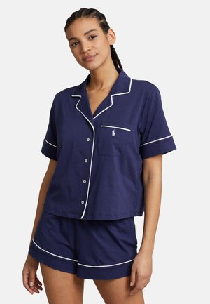 Marineblaue Kurzarm-Pyjama-Serie mit weißen Paspeln, bestehend aus einem Kragen, einer Brusttasche und einer Knopfleiste auf dem Oberteil; Shorts mit ähnlichen Akzenten.