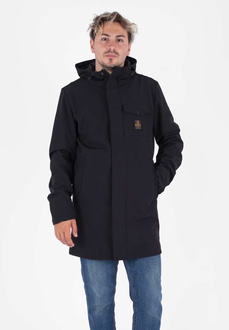 Zwarte waterdichte jas met capuchon, voorkleurige knoopsluiting, twee zijzakken en een borstzak. Bevat een klein logo-opdruk op de borst.