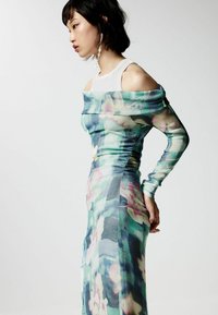 Šaty s kvetinovým potlačou z priesvitného a ľahkého materiálu. Majú dizajn bez ramienok, dlhé rukávy a na bokoch skladanie.