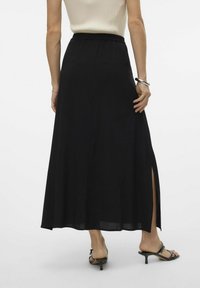 Gonna maxi nera realizzata in tessuto morbido e fluido, con un alto spacco e una vita elastica. Abbinata con sandali neri con cinturini.