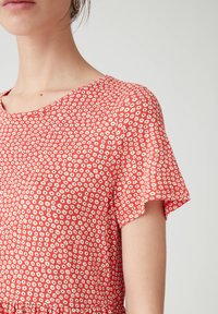 Czerwona koszulka z krótkim rękawem i okrągłym dekoltem, z małym białym wzorem kwiatowym. Miękka w dotyku i luźna w fasonie.