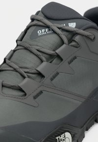 Zapato de senderismo gris oscuro con parte superior de tejido texturizado, cordones elásticos, suela de goma y acentos de logotipo. Punta redondeada y lengüeta acolchada.