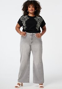 T-shirt noir avec broderie florale blanche, associé à un jean large taille haute gris et des talons beiges à lanières.