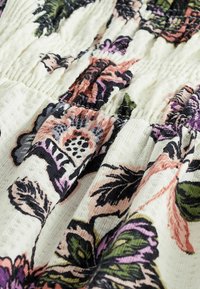 Gros plan sur un tissu blanc texturé avec smocks élastiques et un motif floral multicolore dans des tons rose, vert, violet et noir.
