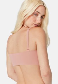 Bralette rose avec des bretelles fines réglables, un design sans coutures et une texture lisse, dotée d'une fermeture arrière simple pour un bon maintien.